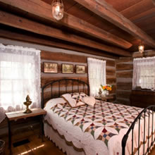 A cozy bed with antique covers in a log cabin room are is one of the accomodations at the Pioneer Trading Post